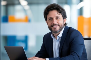 Fototapeta premium Confident businessman in a modern office setting, working on a laptop. He is smiling and appears approachable, reflecting a successful professional environment.