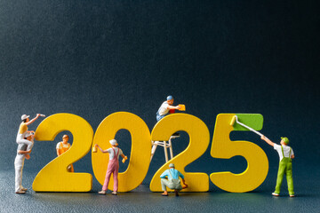 Creative concept of miniature figures painting and constructing the year 2025 in vibrant yellow and...