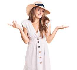 Young beautiful blonde woman wearing summer dress and hat clueless and confused expression with...