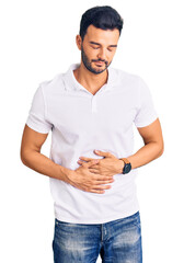 Young handsome hispanic man wearing casual clothes with hand on stomach because indigestion,...