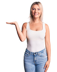 Fototapeta premium Young beautiful blonde woman wearing casual sleeveless t-shirt smiling cheerful presenting and pointing with palm of hand looking at the camera.