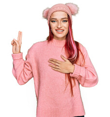 Young caucasian woman wearing casual clothes and wool cap smiling swearing with hand on chest and...