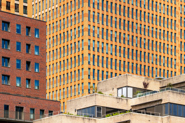 The photo highlights the intricate facade of a series of modern buildings, showcasing diverse textures, colors, and a blend of brick and glass elements unique to contemporary design in Amsterdam