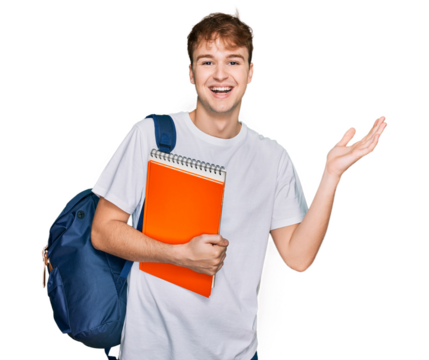 Young caucasian man wearing student backpack and holding books celebrating victory with happy smile and winner expression with raised hands