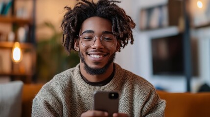 Smiling young man with dreadlocks using smartphone indoors
