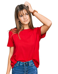 Fototapeta premium Teenager caucasian girl wearing casual red t shirt confuse and wondering about question. uncertain with doubt, thinking with hand on head. pensive concept.