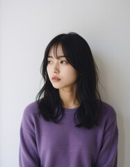 Obraz premium Contemplative Young Asian Woman in Purple Sweater Against a Neutral Background