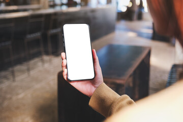 Mockup image of a woman holding and using mobile phone with blank desktop in cafe