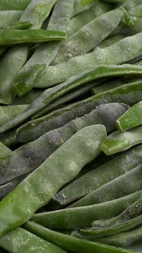 Frozen whole young cranberry bean pods background. Table spin. Vertical video.