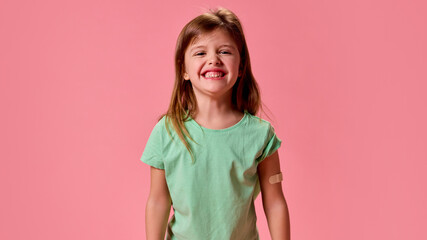 Happy, cheerful smiling and healthy little schoolgirl with patch on hand after vaccination against pastel pink background. against pastel pink background. Concept of healthcare, protection, immunity