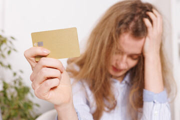 Confused woman holding credit card near laptop at table indoors. Beware of fraud, bad financial deal