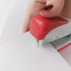 Female hand staples sheets of paper. Stapler with staples.