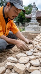 Fototapeta premium Bricklayer skillfully lays brown bricks in a red clay style on a sunny day near a temple, enhancing the structure's beauty and strength