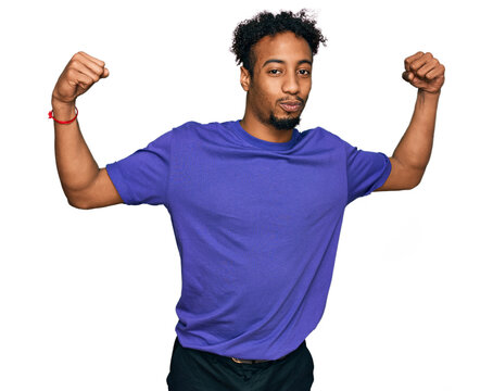 Young african american man with beard wearing casual purple t shirt showing arms muscles smiling proud. fitness concept.