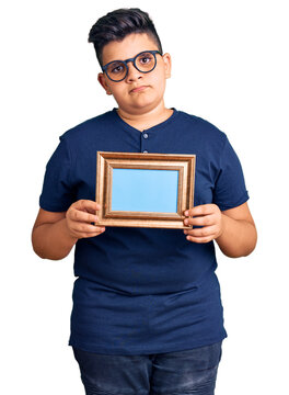Little boy kid holding empty frame thinking attitude and sober expression looking self confident
