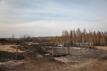 Black ashes on the site of a burnt house with a burnt fence. A completely burnt house after a fire.