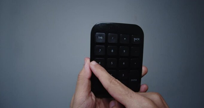 Beautiful slow motion close-up shot of a young man's hand holding a small black calculator or mini computer numeric keypad in front of the camera inside a room with white walls.