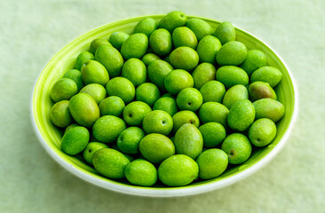 Beautiful kitchen plate with fresh green olives on monochrome green salad background. Olive dish...