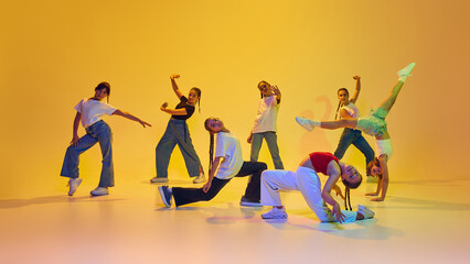 Dynamic image of stylish teen girls wearing casual attire, dancing hip hop, training against yellow...
