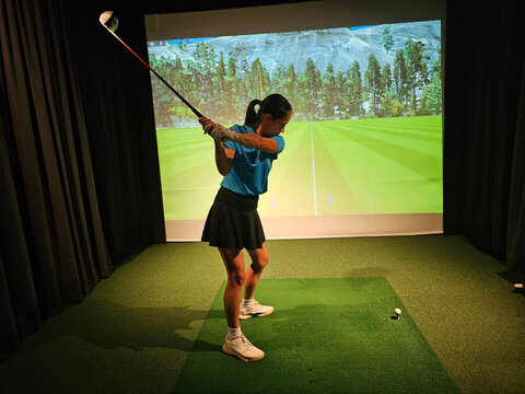 Young golfer practices swing in indoor simulation at a training facility concept