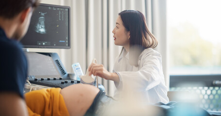 Expectant Couple Attending Prenatal Ultrasound Appointment. Asian Doctor Conducts Scan, Explaining...