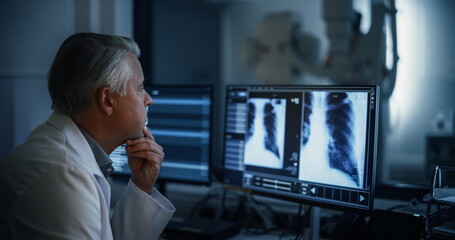 Experienced Radiographer Examines Chest X-rays on Multiple Computer Monitors in a Dark Medical...