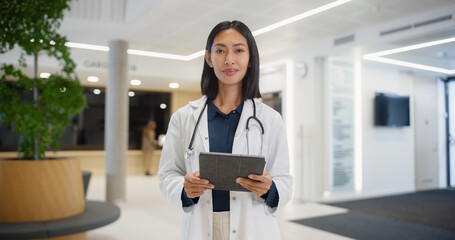 Young Asian Female Doctor in White Coat, with a Stethoscope Around Her Neck, Standing in a Bright...