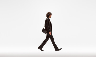 Obraz premium A man walks in the middle of an empty white space. He is wearing black trousers and a jacket with a shoulder bag. It is a cinematic, long shot.