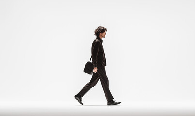 Obraz premium A man walks in the middle of an empty white space. He is wearing black trousers and a jacket with a shoulder bag. It is a cinematic, long shot.