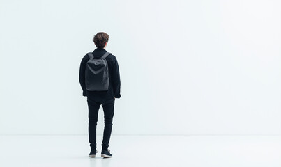 Obraz premium A man walks on the white floor, dressed in black trousers and a jacket with his back to the camera, walking towards an empty space.