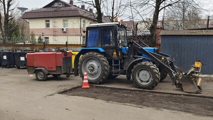 Fototapeta premium On a cloudy spring day, the road service was repairing a hole in the asphalt and temporarily marked the spot with brightly colored plastic posts. A tractor with a compressor trailer stands nearby