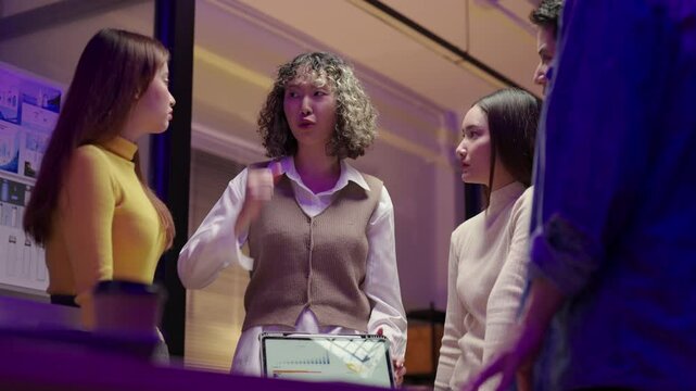 Young Asian business team stacking hands and raising them together and clasping hands after show of teamwork and success, celebrating their achievement with enthusiasm.