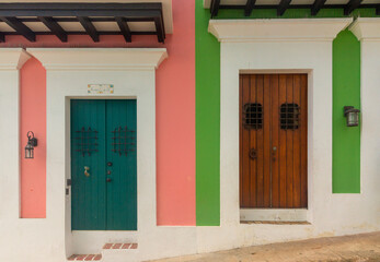 Vibrant and contrasting wooden doors in pink and green colonial buildings showcase the charm and...