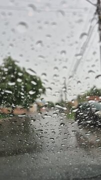 Gotas de chuva caindo no para-brisa do carro, em uma rua da cidade, durante o dia.