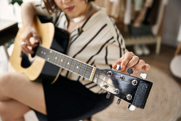 A young woman with curly hair tunes her guitar in a chic apartment filled with natural light.