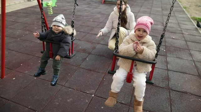 Young woman pushing kids on swing