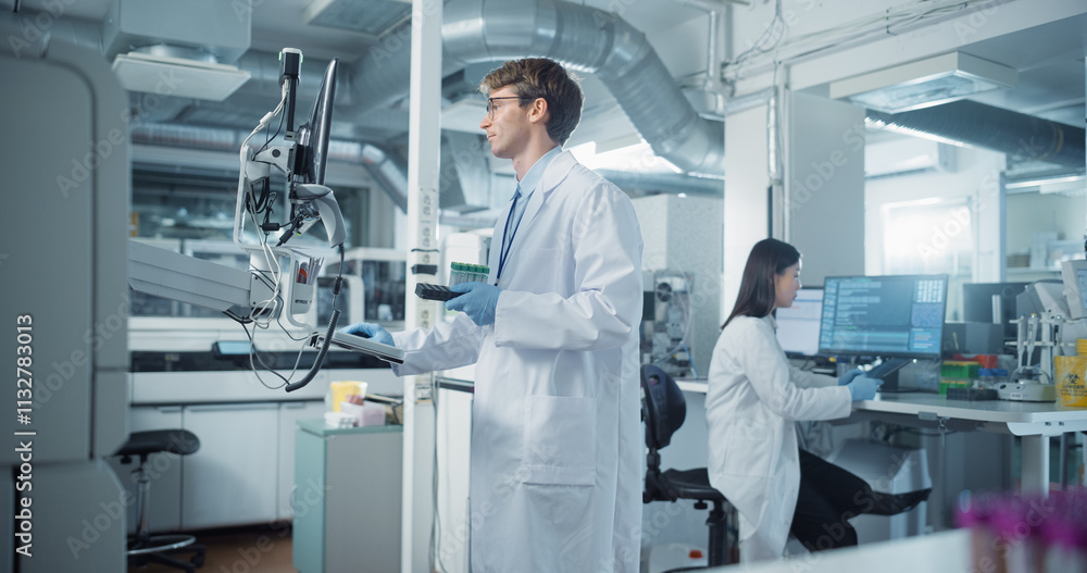 Aufkleber portrait of a young male scientist holding a set of test tubes and using a computer while standing i