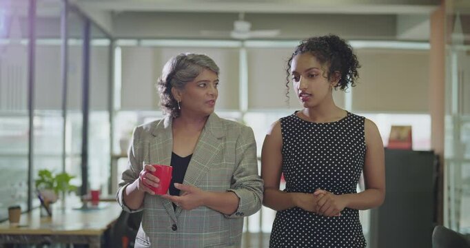 Indian Asian senior boss women lady drink hold coffee cup mug gossip talk indoor work place young adult teen curly hair girl speak share idea listen plan during tea break spend time enjoy job day