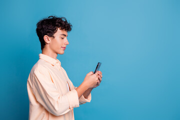 Young man with curly hair interacting with smartphone against blue backdrop in casual style