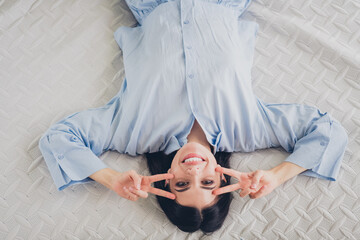 Charming young woman smiling and relaxing on bed in blue sleepwear during a bright morning at home
