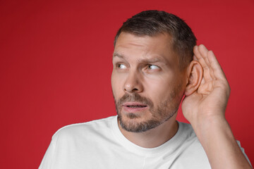Man showing hand to ear gesture on red background