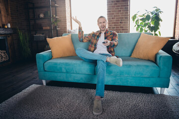 Obraz premium Young man in casual style enjoying a relaxed day indoors on a cozy blue sofa in a stylish loft apartment