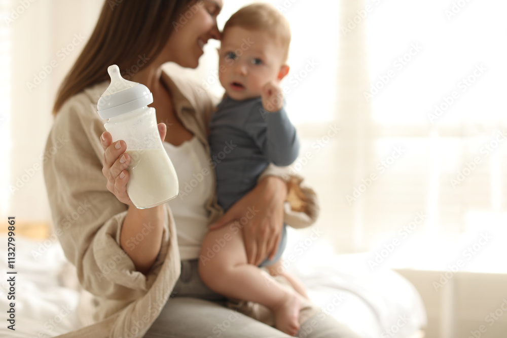 Canvas Prints Mother holding cute little baby and bottle of milk on bed at home, selective focus. Space for text