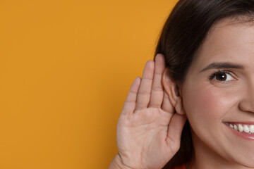 Woman showing hand to ear gesture on orange background, closeup. Space for text