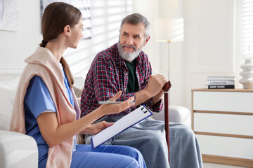 Caregiver examining senior man on sofa indoors. Home health care service