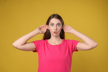 Woman showing hand to ear gesture on dark yellow background