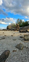 Serene beach setting featuring a rock stacking activity under a blue sky with fluffy clouds