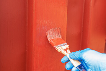 A hand with a brush paints an old iron surface with burgundy paint.