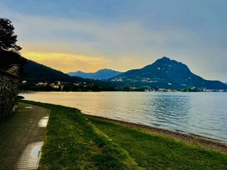 A peaceful lakeside scene during sunset, with golden light illuminating the sky and reflecting on...