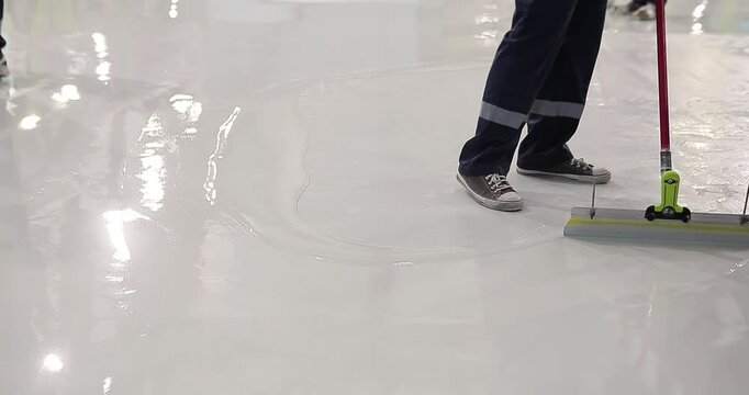 A builder distributes resin flooring material evenly using a Scraper Float. A builder is applying polymer floors using Scraper Float. The process of creating polymer floors